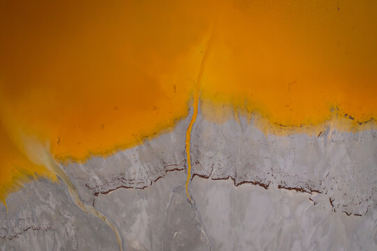 Aerial view of Geamana Poisoned Lake, showing vibrant orange toxic runoff meeting grey sediment in Geamana, Alba County, Romania.