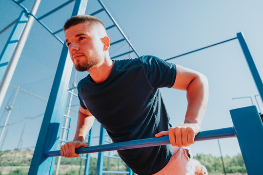 Young man performs a bodyweight push-up on parallel bars focused on upper body strength. Outdoor calisthenics training on fitness bars in a sunny park setting.