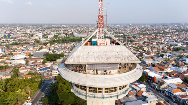 Aerial view of the observation tower with visitors on the viewing deck, surrounded by the dense urban landscape of the city in Semarang, Central Java, Indonesia.