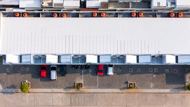 Aerial view of a long building with a white corrugated metal roof, orange water tanks, and parked cars in the parking lot in Semarang, Central Java, Indonesia.