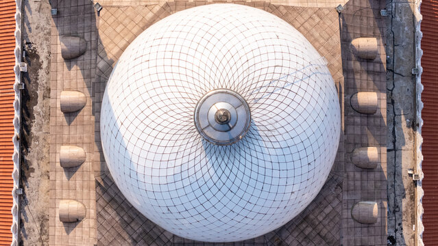 Aerial view of the intricate white dome of the Great Mosque of Central Java, featuring a geometric pattern and surrounding tiled roof, in Kecamatan Gayamsari, Jawa Tengah, Indonesia.