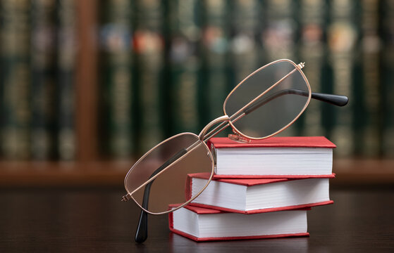 Reading glasses and miniature books against a bookshelf background