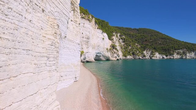 Vertical drone crane up along white cliff wall copy space, Vignanotica beach, Gargano, Puglia Italy. 4K empty wild shore, turquoise sea and distant caves