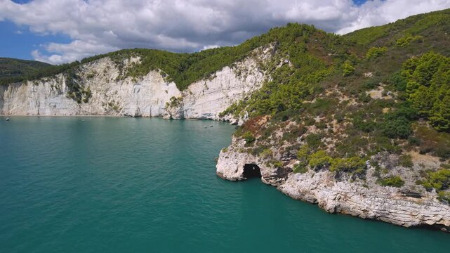 Pristine Vignanotica Beach Aerial drone descent to sea cave entrance in vertical white cliffs of Gargano Italy. Untouched wild nature of Puglia National Park 4K