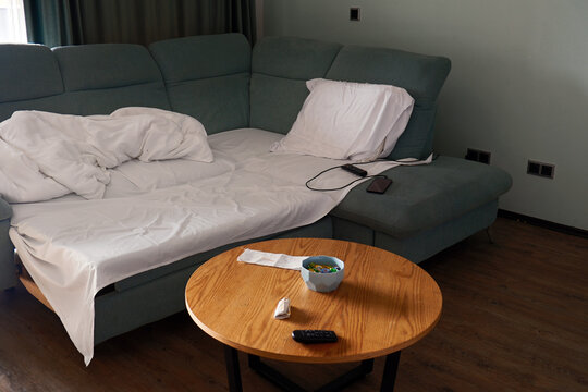Messy unmade sofa bed with white sheets and wooden coffee table in modern living room