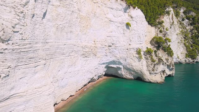 Pristine nature Vignanotica Beach Gargano National park Puglia Italy. low drone flyby vertical white cliffs cove anchored boats pine trees turquoise sea Cinematic low-altitude aerial video
