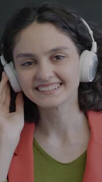 Portrait of cheerful young woman listening to music with headphones dancing on black background. Youth culture and entertainment concept.