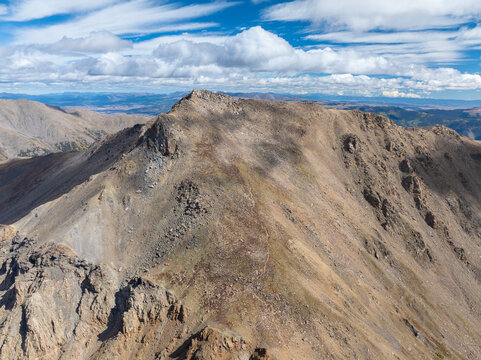 Aerial view of Mount Harvard with its rugged rocky peak and steep slopes under a bright blue sky with scattered clouds in Buena Vista, Colorado, United States.