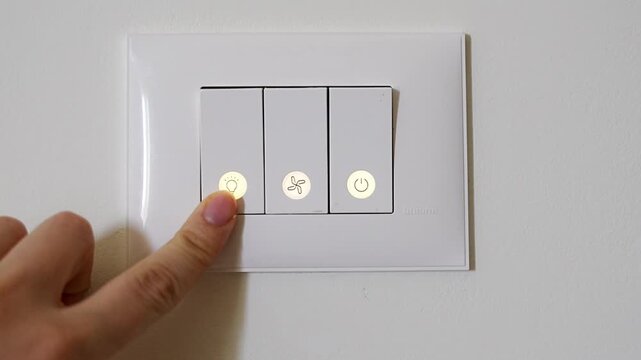 Woman pressing touch button to turn on indoor light on modern wall control panel. Illuminated switch shows activation of home lighting system