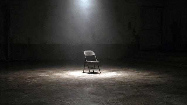 Single empty chair under a spotlight in a dark abandoned room creating a concept of isolation, absence, waiting and loneliness