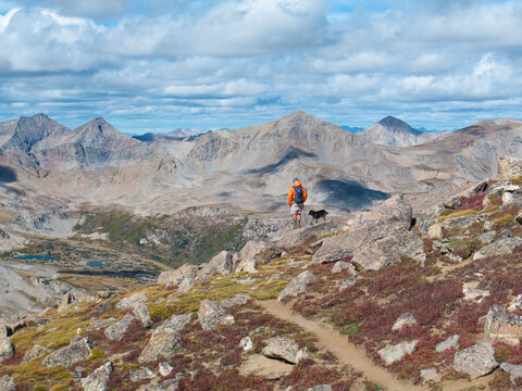 Aerial view of a hiker and their dog standing on a rocky trail overlooking the rugged peaks of Mount Harvard in Buena Vista, Colorado, United States.