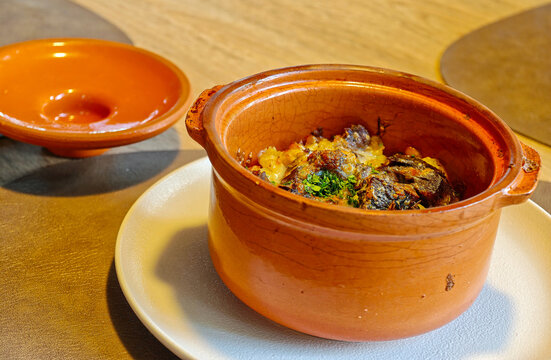 Hot meat dish served in a clay pot with baked potatoes or vegetables, sprinkled with herbs.