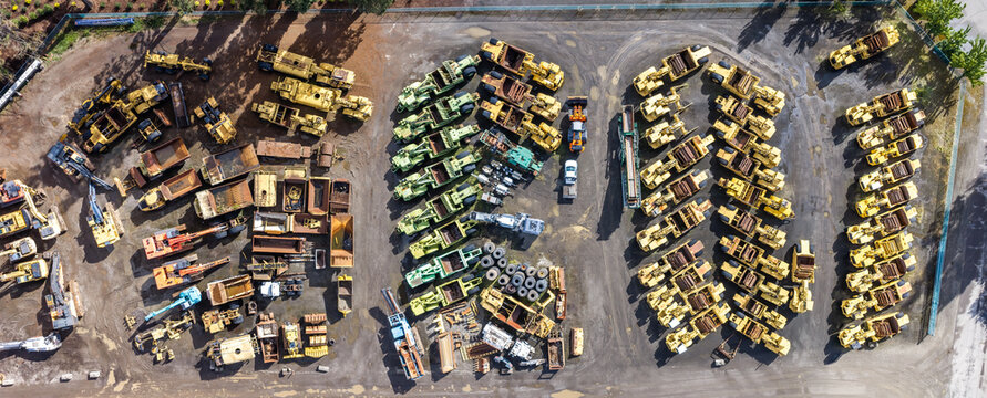 Aerial view of a large industrial yard filled with various heavy construction machinery, including excavators, loaders, and dump trucks, arranged in rows in Woodburn, Oregon, United States.