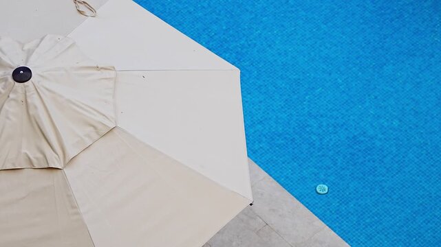 Luxury outdoor swimming pool with sun umbrellas viewed from above at a modern resort. Summer vacation, relaxation and premium hospitality lifestyle.