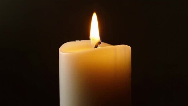 White candle burns with a gently flickering flame against a dark background