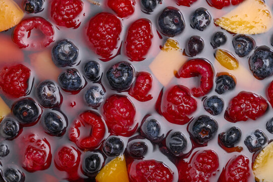 Fruits immersed in thickening jelly for a macro dessert, raspberries and blueberries