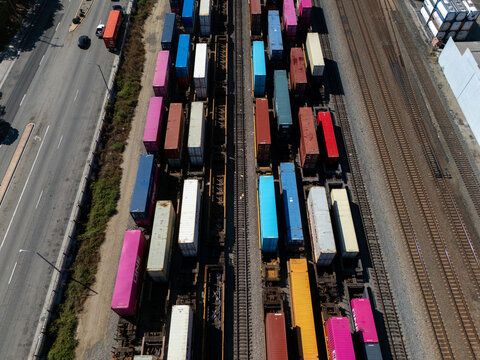 Aerial view of a freight train loaded with colorful shipping containers on parallel tracks next to a highway in Carson, California, United States.