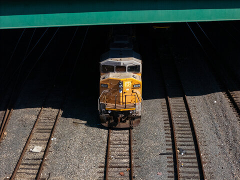 Aerial view of a yellow locomotive traveling on train tracks under a bridge in Carson, California, United States.