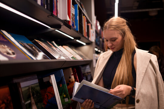 Book lover. Curious young woman pupil student visit public library read literature look through selected volume turn pages with interest search learning information for university degree college essay