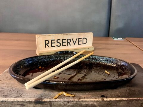 Empty sizzler hot plate with wooden chopsticks and reserved sign on table in restaurant