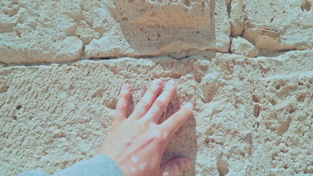 hand with distinct vitiligo touching an ancient, weathered stone wall