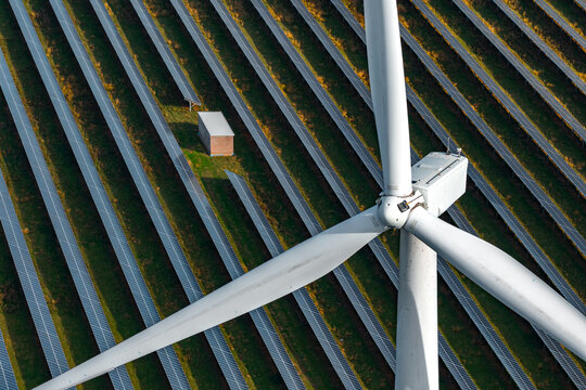 Aerial view of Chelveston Renewable Energy, BESS, featuring a large wind turbine and rows of solar panels in the green landscape of Chelveston, England, United Kingdom.