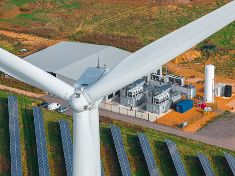 Aerial view of Chelveston Renewable Energy BESS facility featuring a large wind turbine, rows of solar panels, and battery storage units in Chelveston, England, United Kingdom.