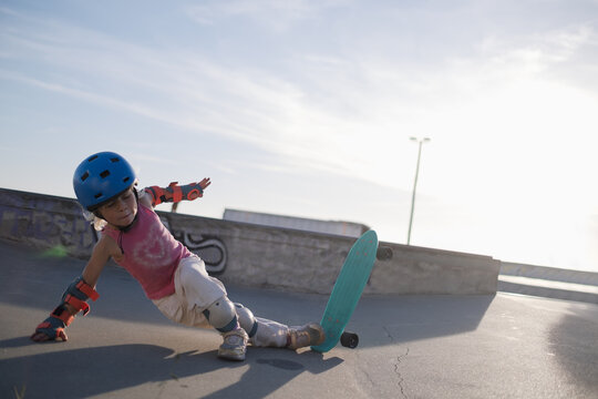 Little Girl in Helmet and Protective Pads Falling Off Penny Board at Skatepark