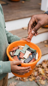 Child holding orange pumpkin bucket while adult hand offers candy on autumn porch steps