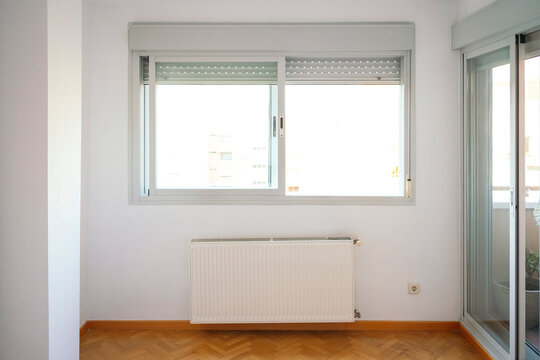 Empty renovated room with window, radiator and parquet floor