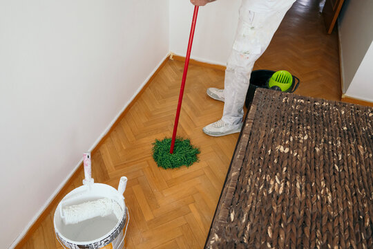 Professional painter cleans parquet floor after wall painting
