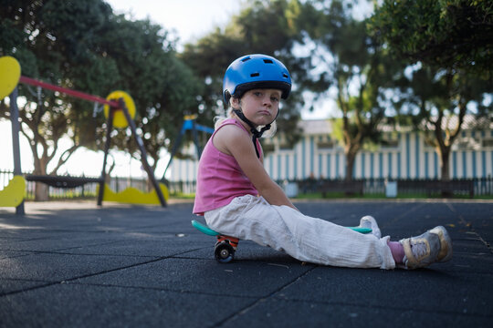 Cute Little Girl in Blue Helmet Sitting on Penny Board at Playground Outdoors