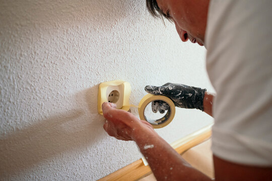 Professional painter masking electrical outlet during wall renovation