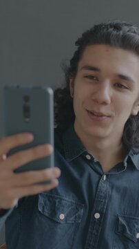 Joyful Hispanic man making online video call with smartphone chatting on gray background. Virtual meeting and communication concept.