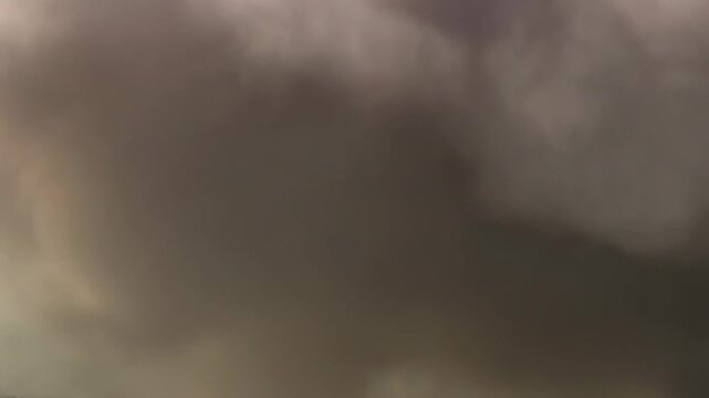 Large gray clouds shift across a pale blue sky in warm changing sunlight