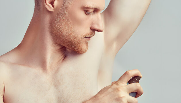 Close up shot of a shirtless man with a beard applying aerosol deodorant to his underarm against a gray background. Clean and minimal look. Perfect for men's grooming advertisements.