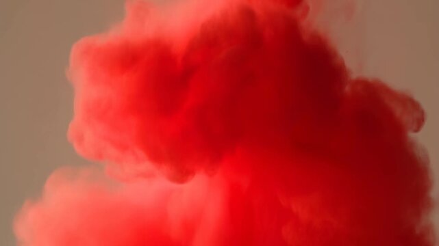Red ink cloud billows and spreads through liquid against a plain beige background