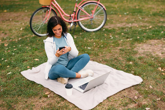 Woman using smartphone and laptop on blanket in park
