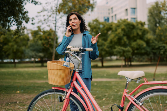 Woman talking on smartphone beside bicycle in park