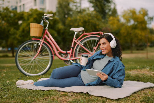 Woman reclining with coffee and tablet beside bicycle