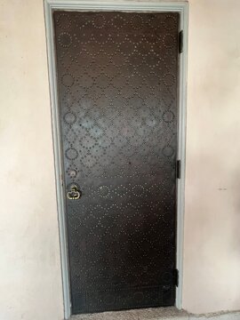 Old dark metal door decorated with studs forming geometric patterns, featuring an antique brass door knocker and weathered architectural details.