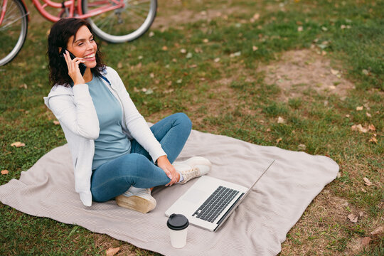 Woman talking on phone working remotely in park