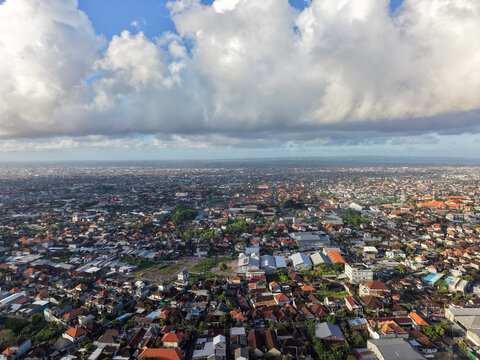Aerial panoramic view of Denpasar city and dense urban neighborhoods under dramatic clouds in Bali