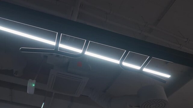 Dynamic upward view moves beneath curved monkey-bar handles and bright linear ceiling lights in a contemporary gym.