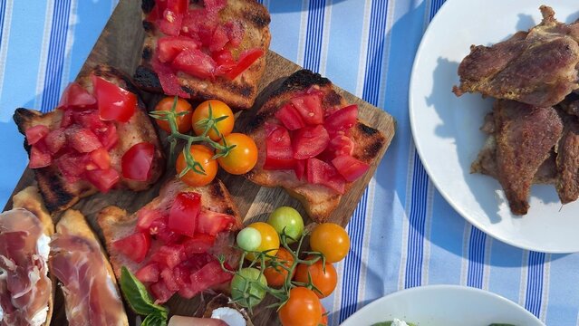 Toasted bread slices topped with chopped red tomatoes and basil on a wooden board, accompanied by cherry tomatoes and fried chicken on a white plate