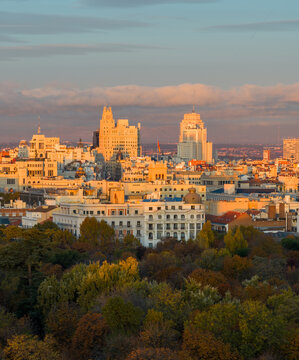 Aerial view of El Retiro Park with the Madrid skyline glowing in the warm sunset light, featuring historic buildings and lush autumn trees in Madrid, Community of Madrid, Spain.