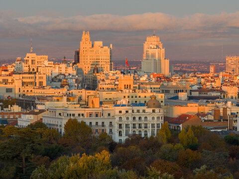 Aerial view of El Retiro Park and the historic skyline of Madrid during golden hour, with warm sunlight illuminating the rooftops and architecture, Madrid, Community of Madrid, Spain.
