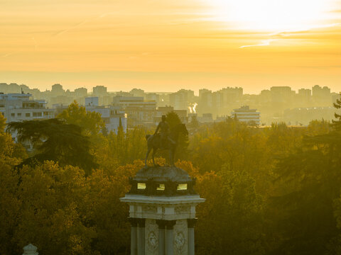 Aerial view of the Monument to Alfonso XII in El Retiro Park surrounded by autumn trees during golden hour with the city skyline in the background in Madrid, Community of Madrid, Spain.