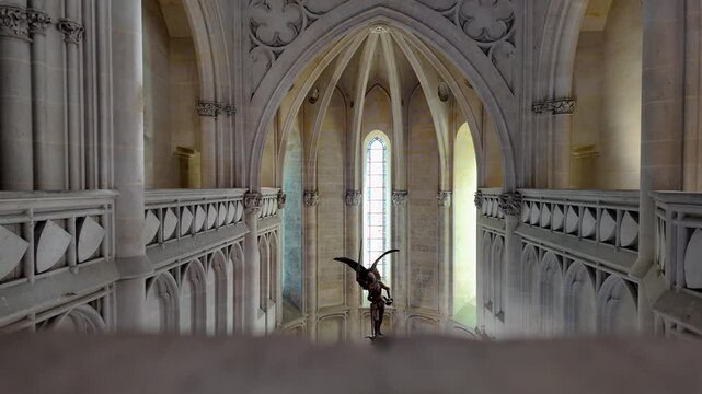 Slow motion forward movement reveals a church statue framed by Gothic arches, carved stone railings and a tall stained glass window at Ch&acirc;teau de Pierrefonds