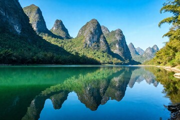 Fototapeta premium Serene mountain landscape with clear lake reflecting karst peaks under blue sky